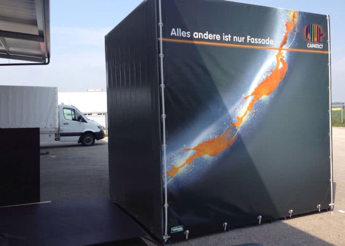 Das Bild zeigt einen Container der Firma Capatect, der als Lagercontainer verwendet wird. Die Planen, die den Container umgeben, sind mit einer digitalen Druckvorlage bedruckt und bieten eine effektive Werbefläche für das Unternehmen. Der Container ist mit einem Reißverschluss ausgestattet, um einen schnellen und einfachen Zugang zum Lagergut zu ermöglichen. Mit diesem Container kann Capatect seine Produkte sicher und effektiv lagern und gleichzeitig Aufmerksamkeit für das Unternehmen generieren.
