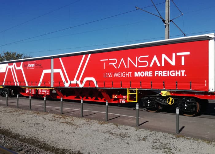 Das Bild zeigt einen Zug-Waggon mit einer seitlich verschiebbaren Schiebeplane der Firma Transant. Das Unternehmen bietet mit diesem Transporter eine effiziente Möglichkeit, Güter sicher und geschützt zu transportieren.