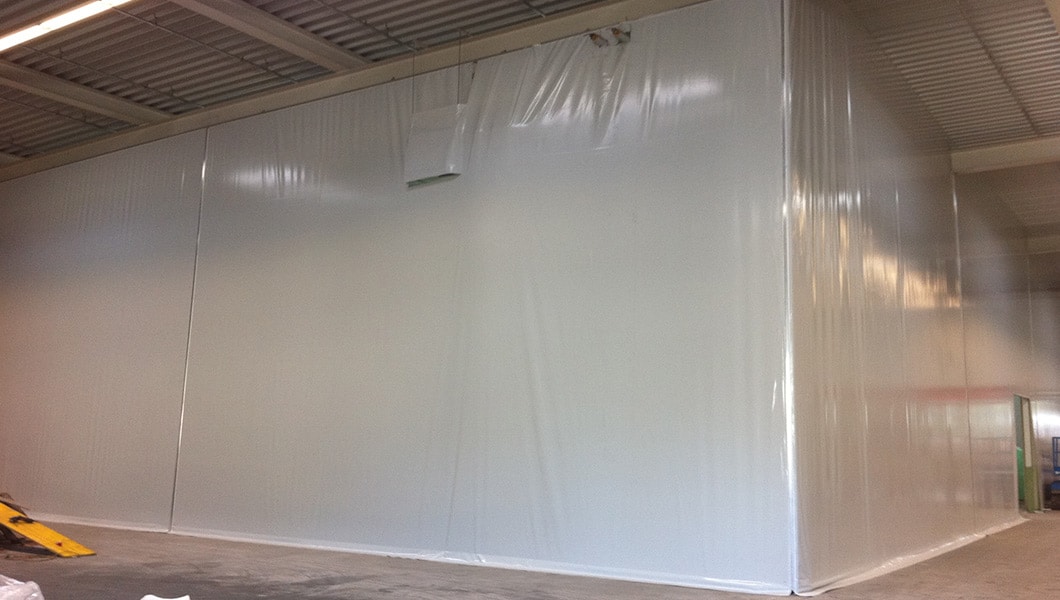 Das Bild zeigt eine Lagerhalle bei der Firma Steinbacher mit einer PVC-Planenabtrennung. Die Abtrennung ermöglicht es, Lagerbereiche effektiv zu organisieren und schützt die gelagerten Waren vor Witterungseinflüssen.