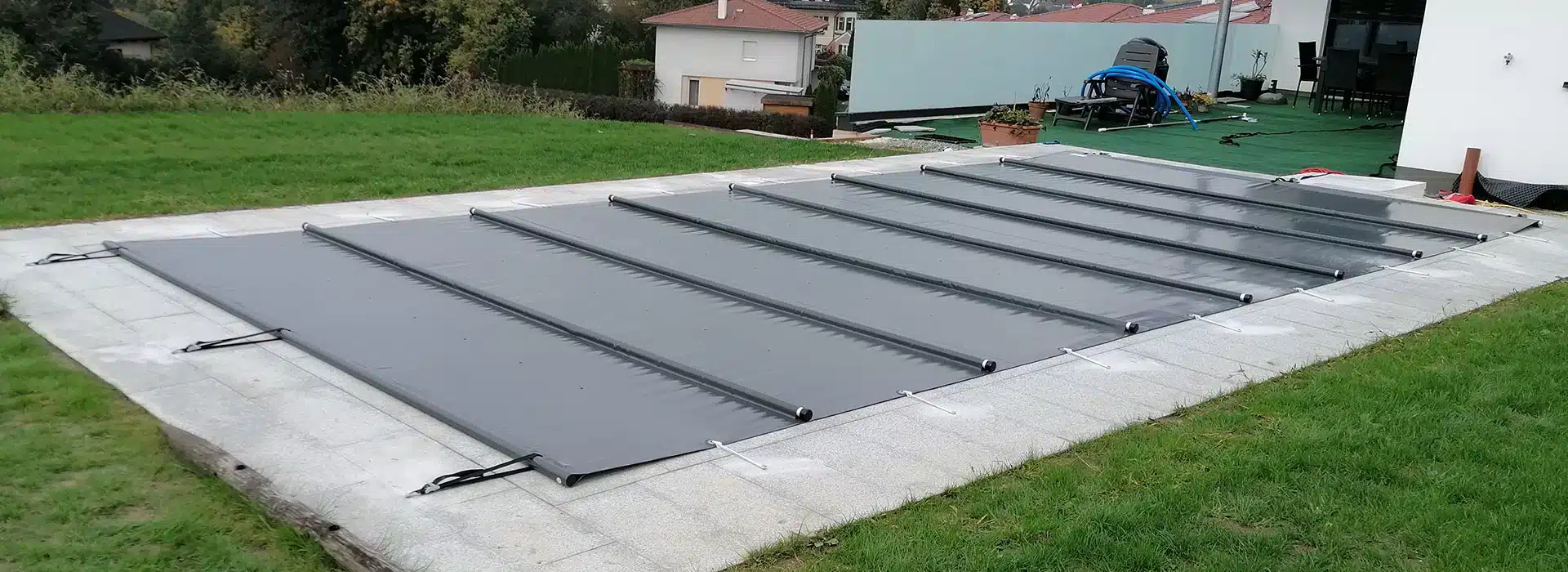 Das Bild zeigt einen Außenpool mit einer Rollplane, die das Becken bedeckt und aus robustem Material besteht. Die Rollplane wird von Karoplan angeboten, um Kunden dabei zu helfen, ihren Pool sauber und gepflegt zu halten.