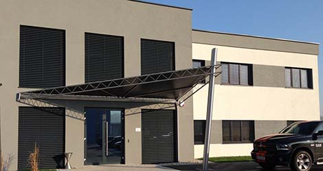 Ein schwarzer PVC-Sonnenschutz spannt sich über den Eingangsbereich, bietet effektiven Schutz vor direkter Sonneneinstrahlung und verleiht ein modernes Aussehen.